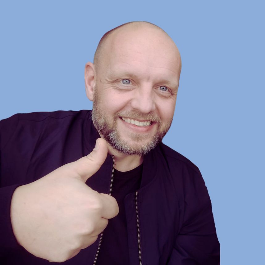 Ein Mann mit kahlk&ouml;pfigem Haar und Bart zeigt Daumen hoch mit einem L&auml;cheln vor einem blauen Hintergrund.